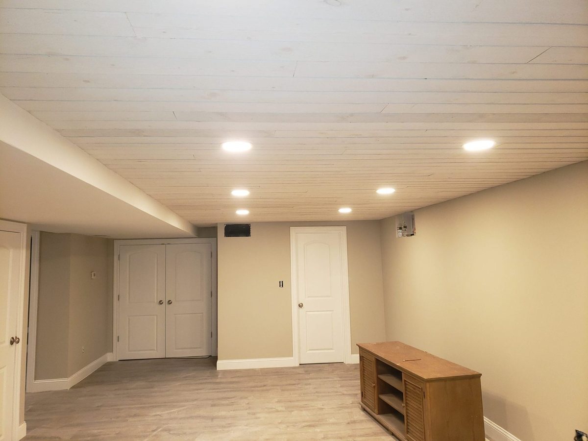 Finished basement with white plank ceiling, recessed lights, gray walls, white doors and laminate floor