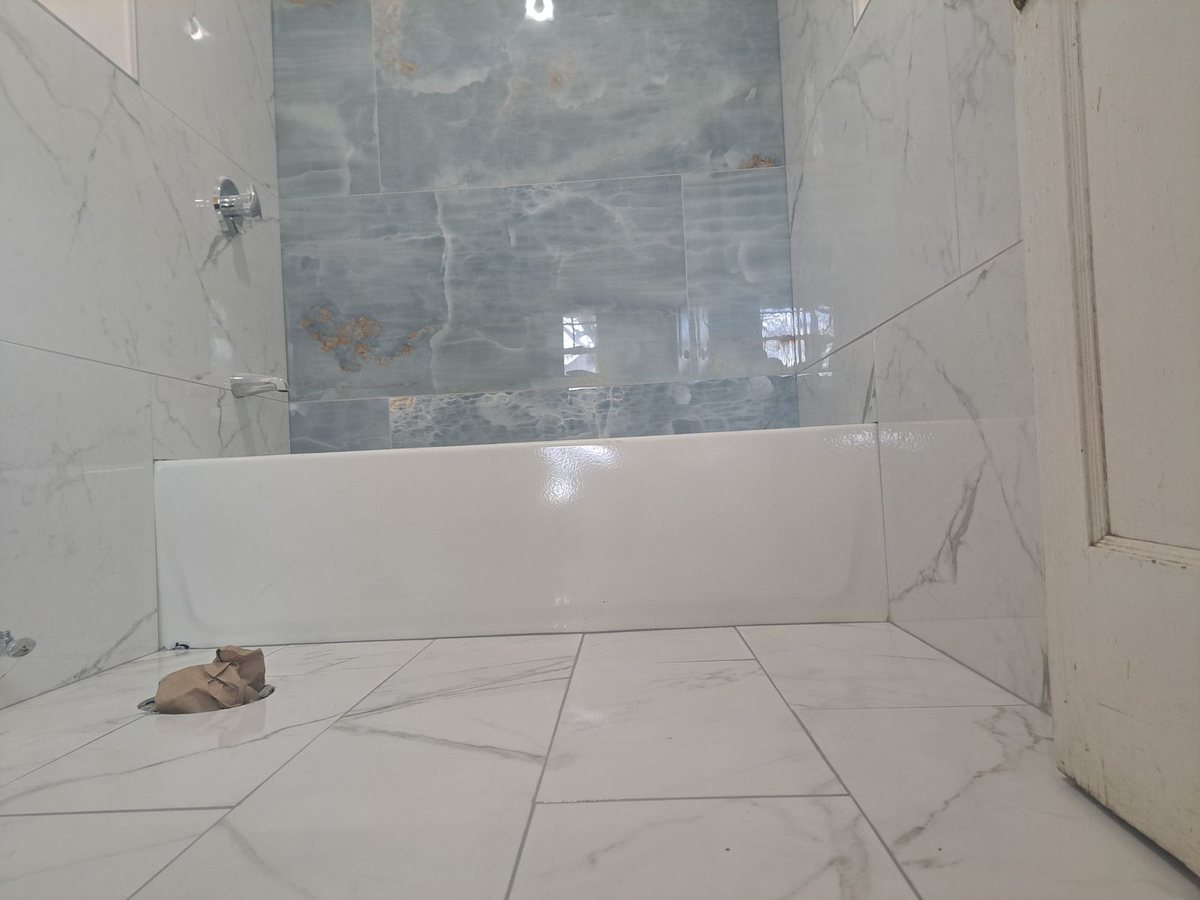 Bathroom with marble-look porcelain tile on walls and floor, white tub and shower fixture
