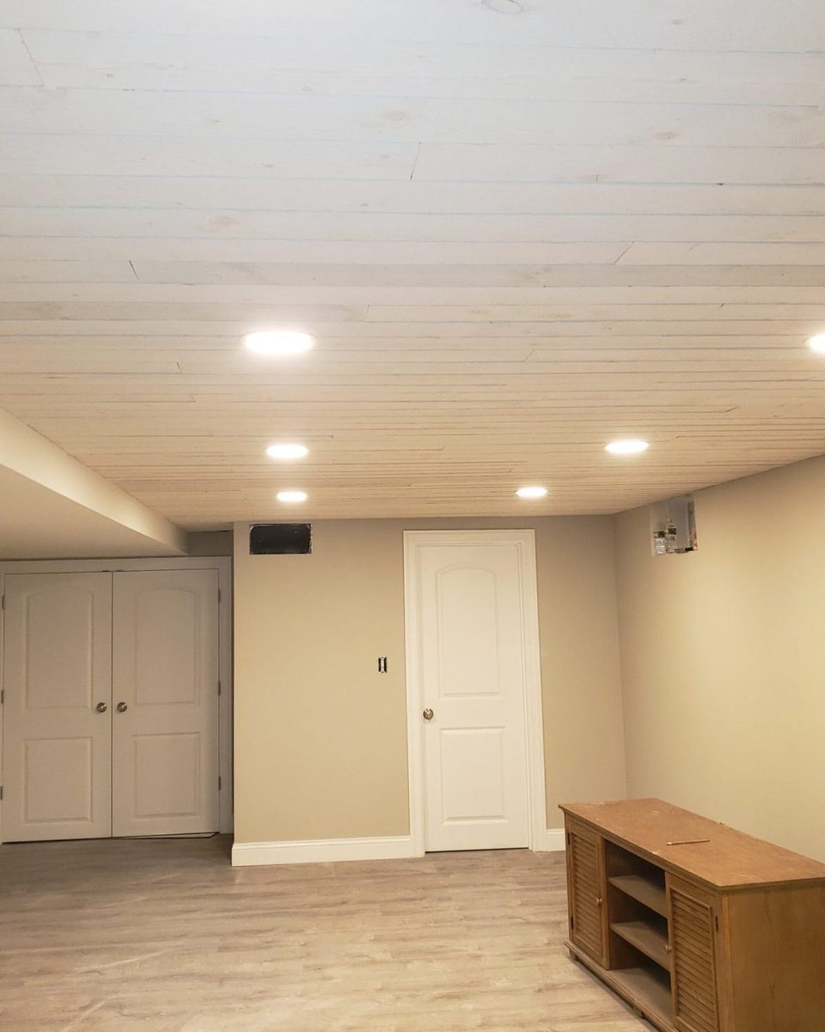 Finished basement with white plank ceiling, recessed lights, gray walls, white doors and laminate floor