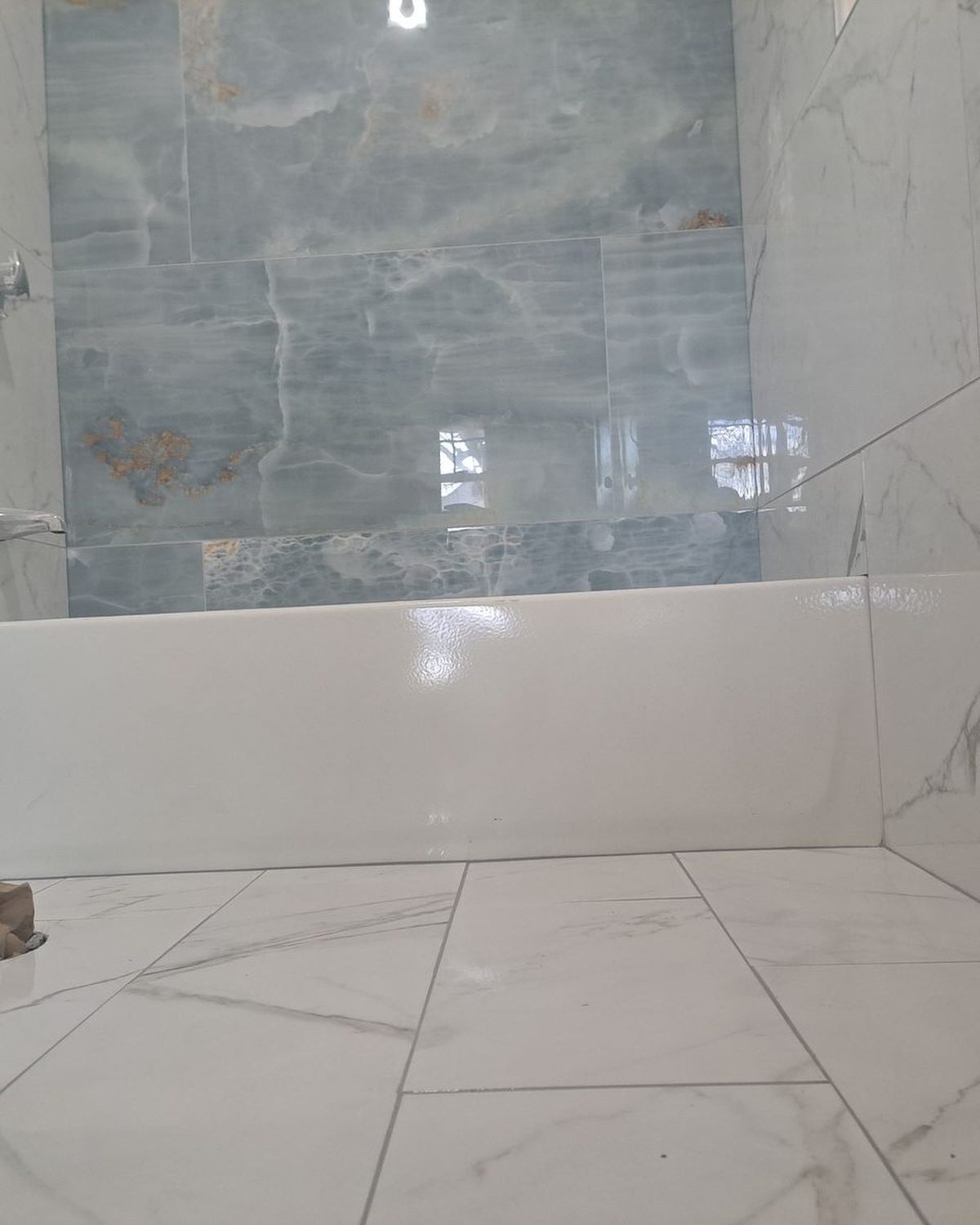 Bathroom with marble-look porcelain tile on walls and floor, white tub and shower fixture